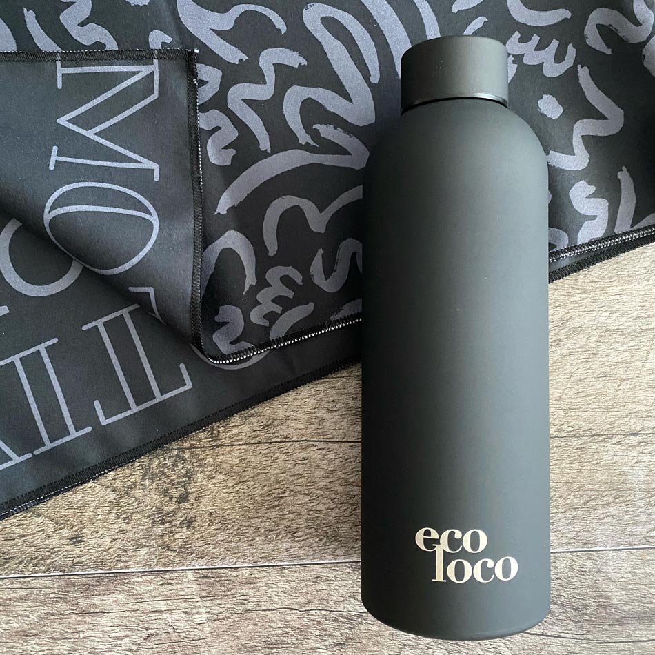 Bouteille d'eau noire carbone en acier inoxydable sur un fond de bois et une serviette de sport en microfibre