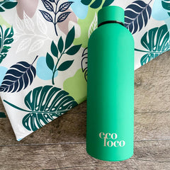 Bouteille d'eau verte en acier inoxydable sur un fond de bois et une serviette de sport en microfibre au motif de feuilles tropicales