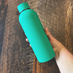 Une bouteille d'eau réutilisable en acier inoxydable de couleur vert turquoise au dessus d'une planche en bois. 