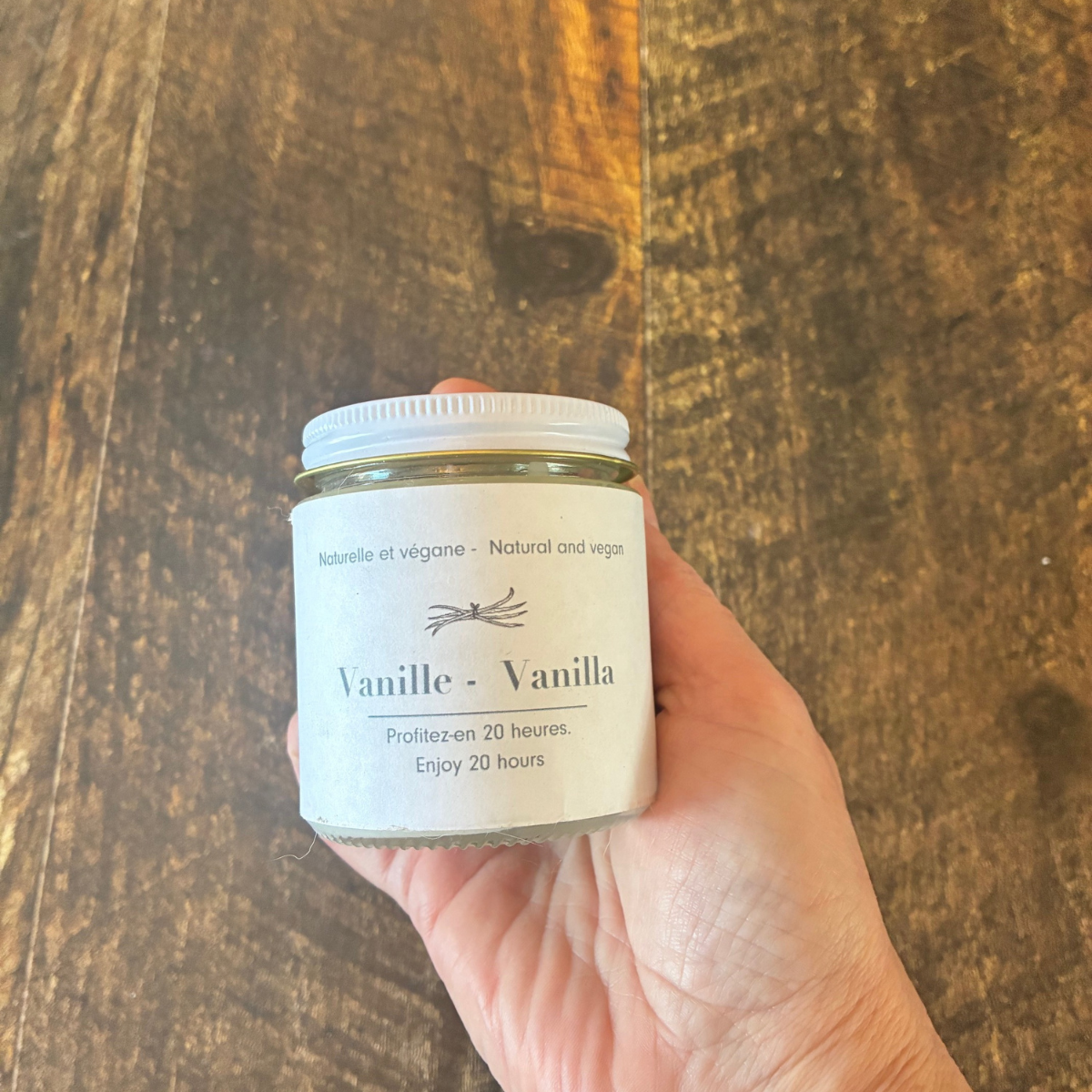 Chandelle en cire de soya et mèche de bois à la vanille tenue dans une main. 