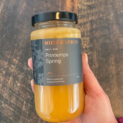 Miel de printemps brut des Miels d'Anicet fait au Québec tenu dans une main au-dessus d'une planche de bois. 