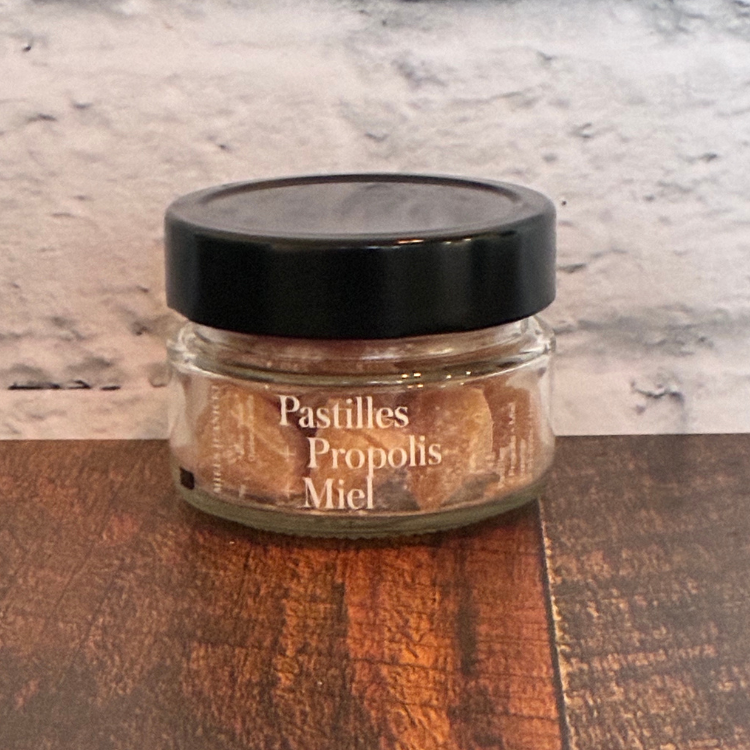 Pot en verre de pastille de propolis et miel des Miels d'Anicet déposé sur une planche de bois