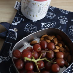 Plant en acier inyxidable contenant des raisins et des amandes déposé sur un napperons à motifs noir et accompagné d'un contenant isolant. 