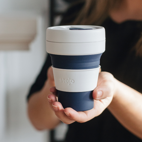 tasse rétractable réutilisable bleu et blanche tenu dans une main de femme avec un arrière plan flou. 
