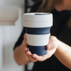 tasse rétractable réutilisable bleu et blanche tenu dans une main de femme avec un arrière plan flou. 